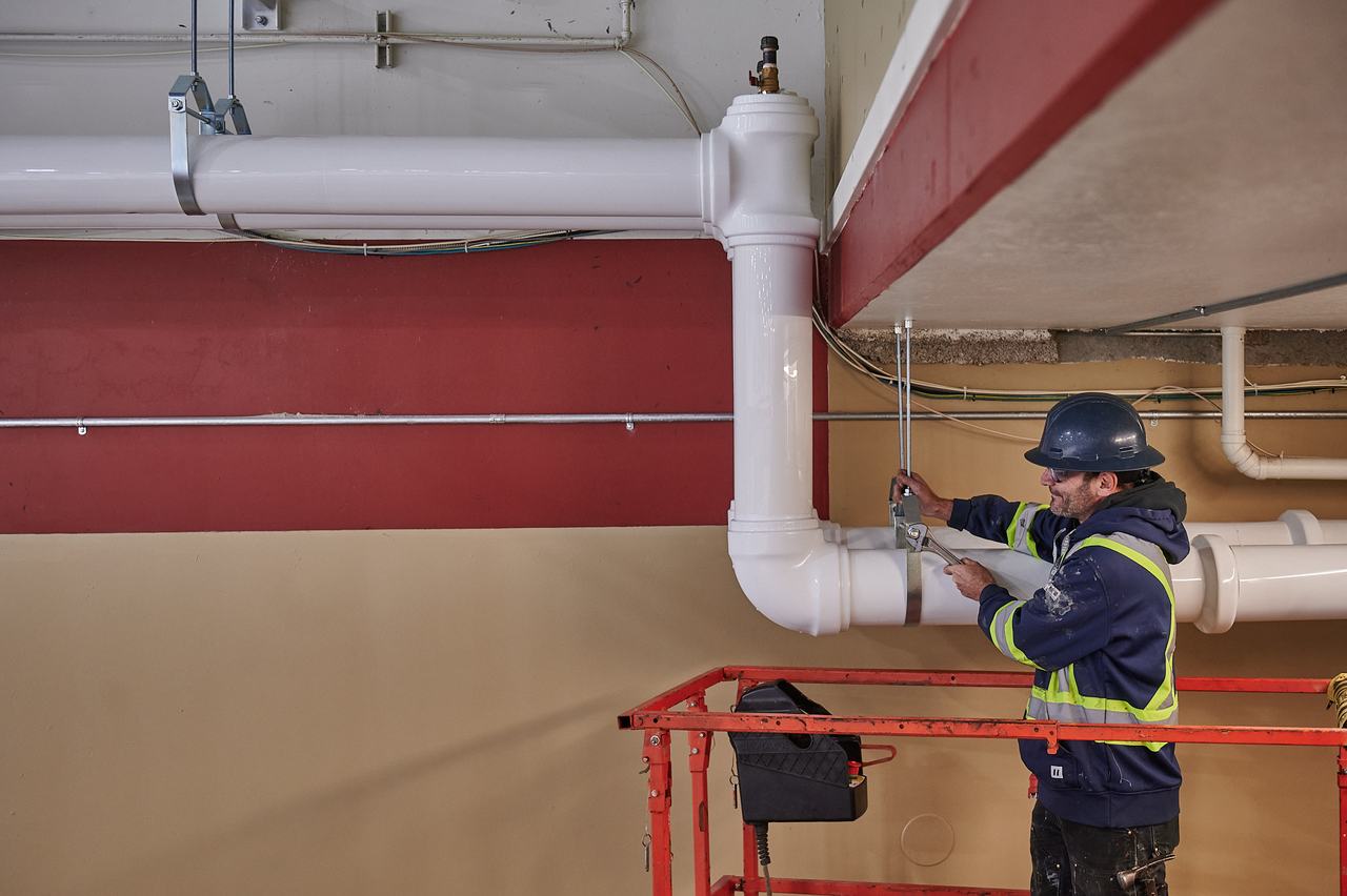Waywest plumber installing large-diameter piping from a lift at the Parksville arena