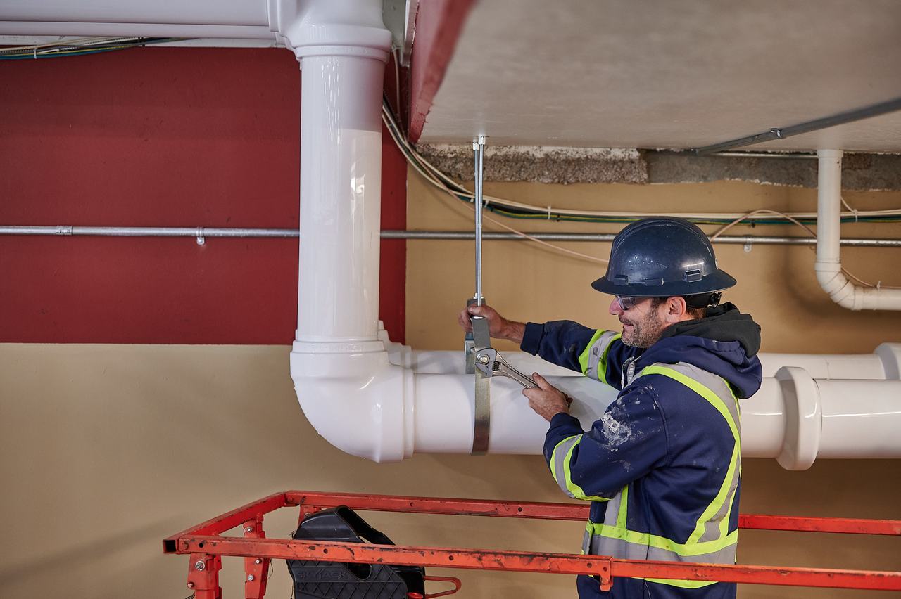 Waywest plumber securing a pipe hanger overhead at the Parksville arena