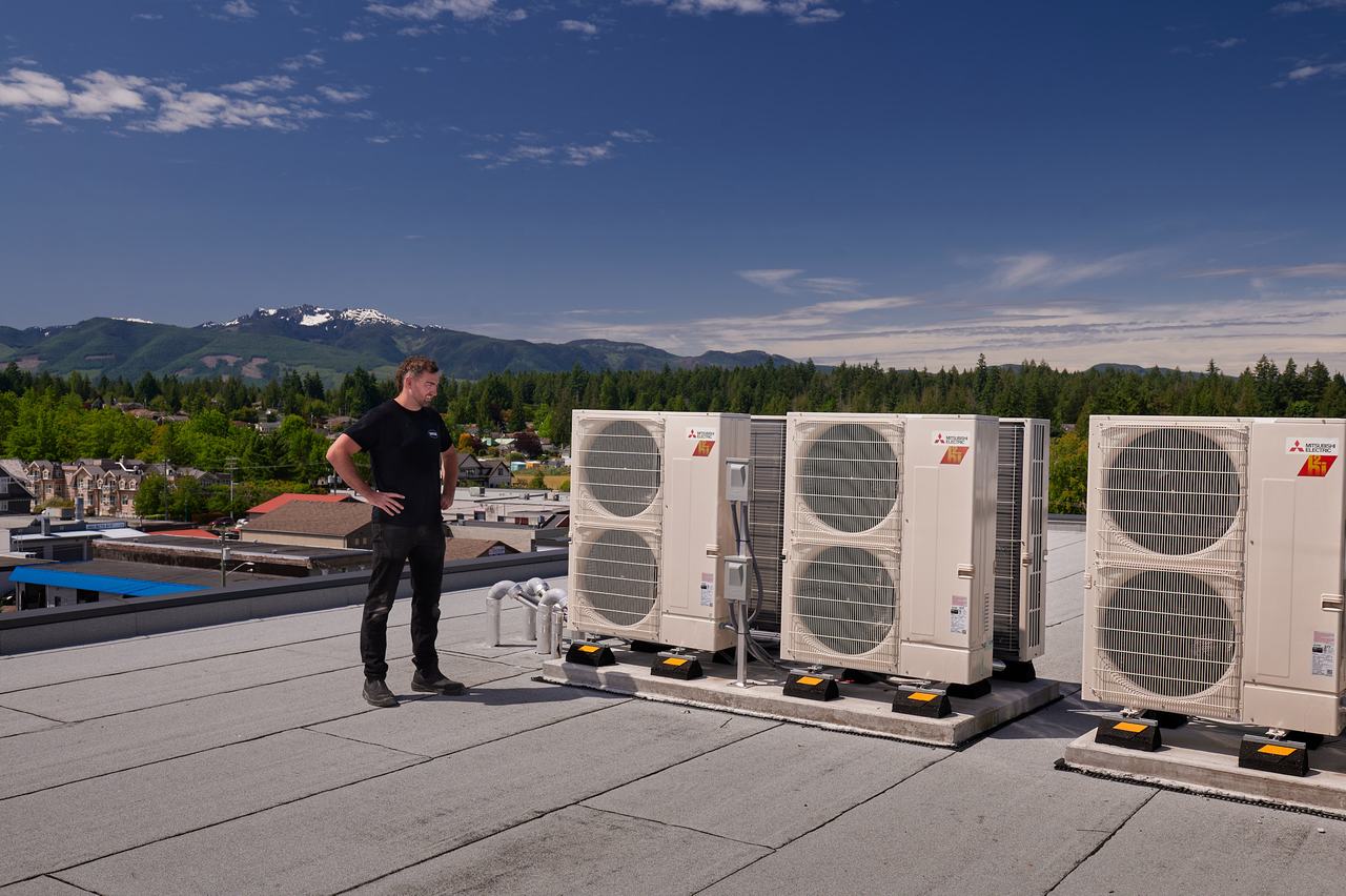 Waywest technician with rooftop heat pump condensers on a Qualicum Beach building