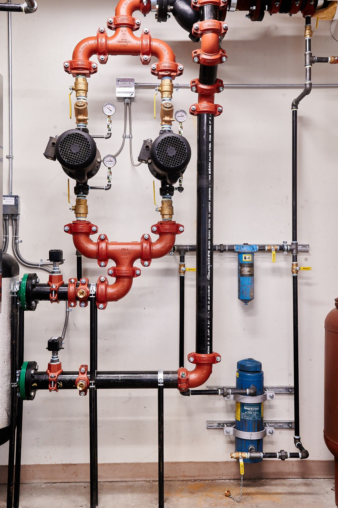 Hydronic circulator pumps and red-painted heating piping in a commercial boiler room