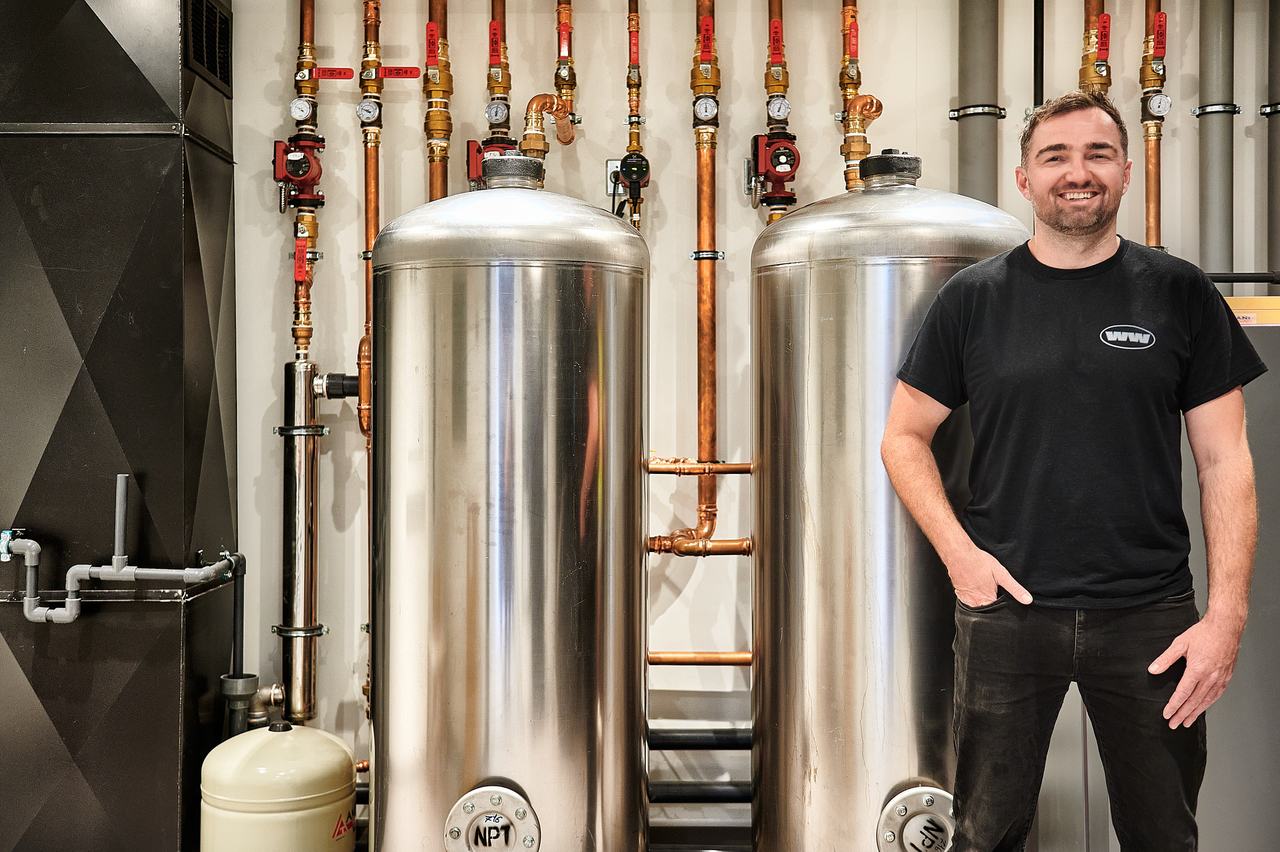 Luke Norman, owner of Waywest Mechanical, beside hot water storage tanks in a Qualicum Beach mechanical room