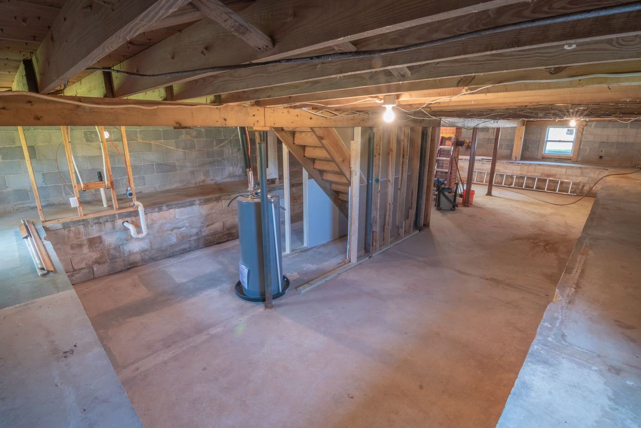 Unfinished basement with exposed pipes and a water heater