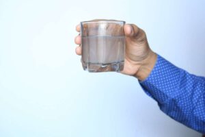 A hand holding a glass of cloudy water - one of the signs of a broken water line that Waywest Mechanical can help repair.