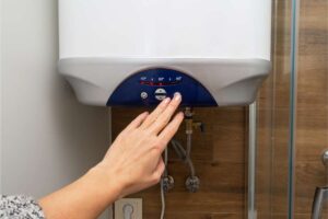A hand pressing a button on a tankless water heater.
